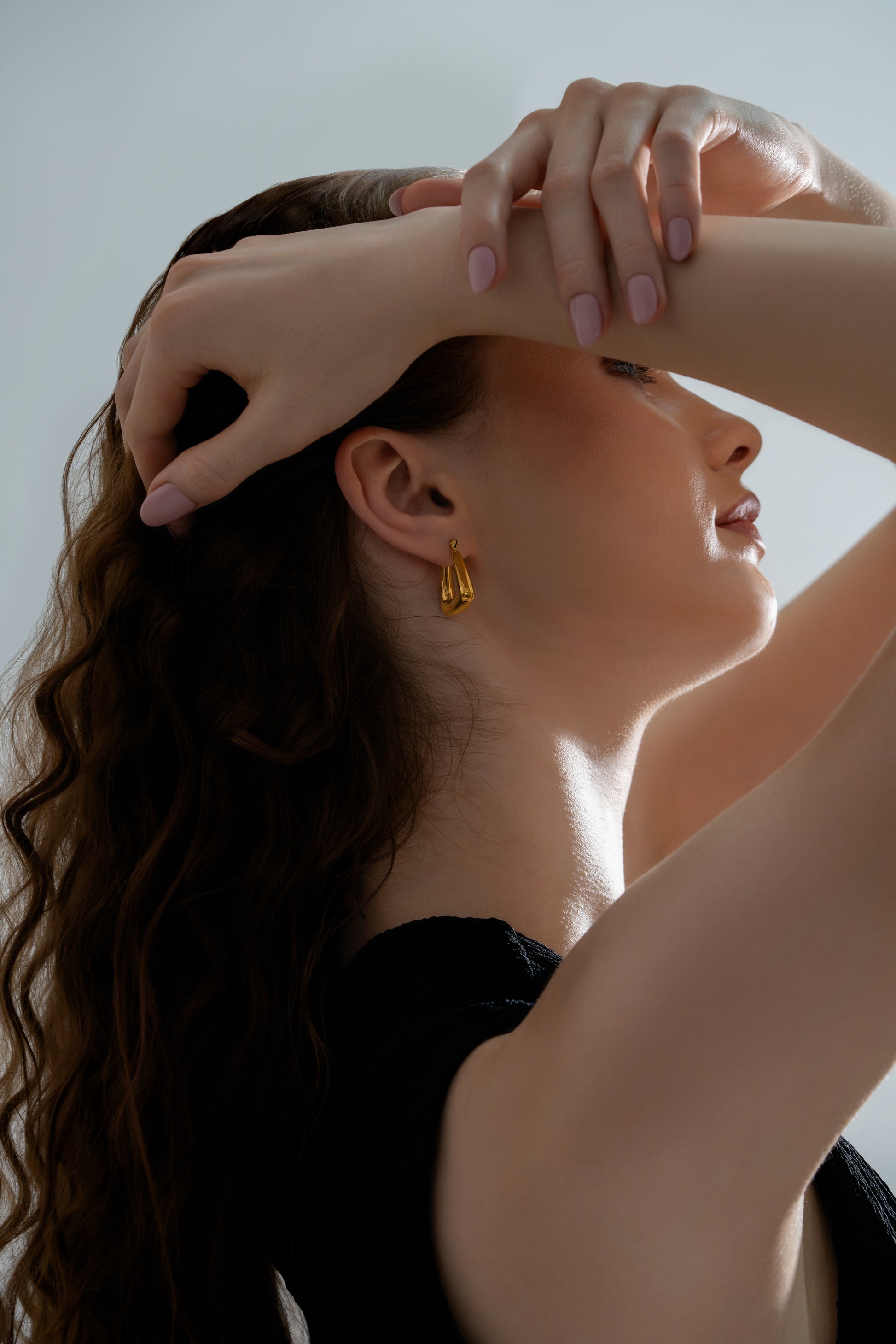 Triangular Hoop Earrings worn by model with hair swept back, emphasizing their unique shape and glossy gold finish.