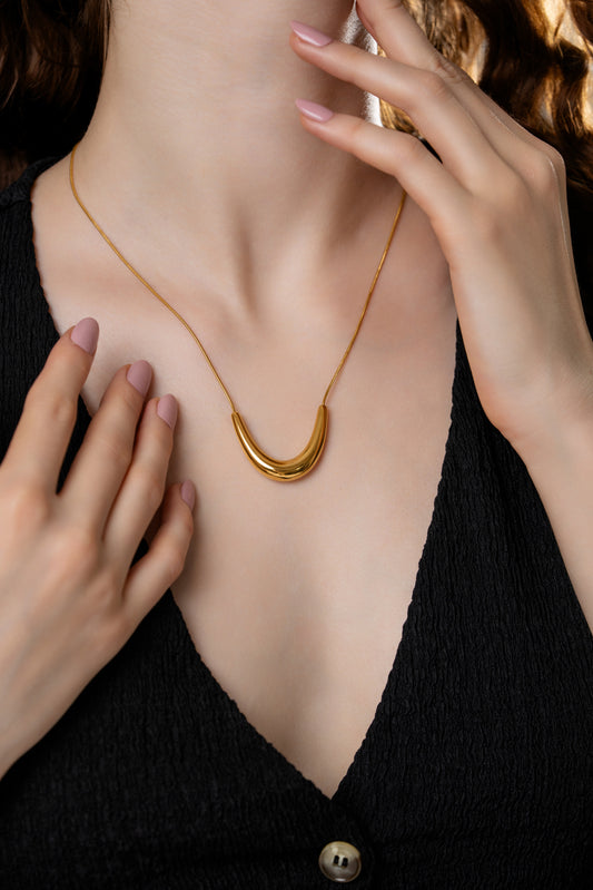 The Arc gold necklace worn with a deep V-neck black top, showcasing its elegant curved pendant and refined minimalist design.