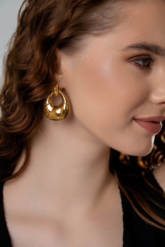Model wearing Twirléa Gold Hoops, showcasing their elegant drop shape and glossy gold tone, perfect for upscale fashion looks.
