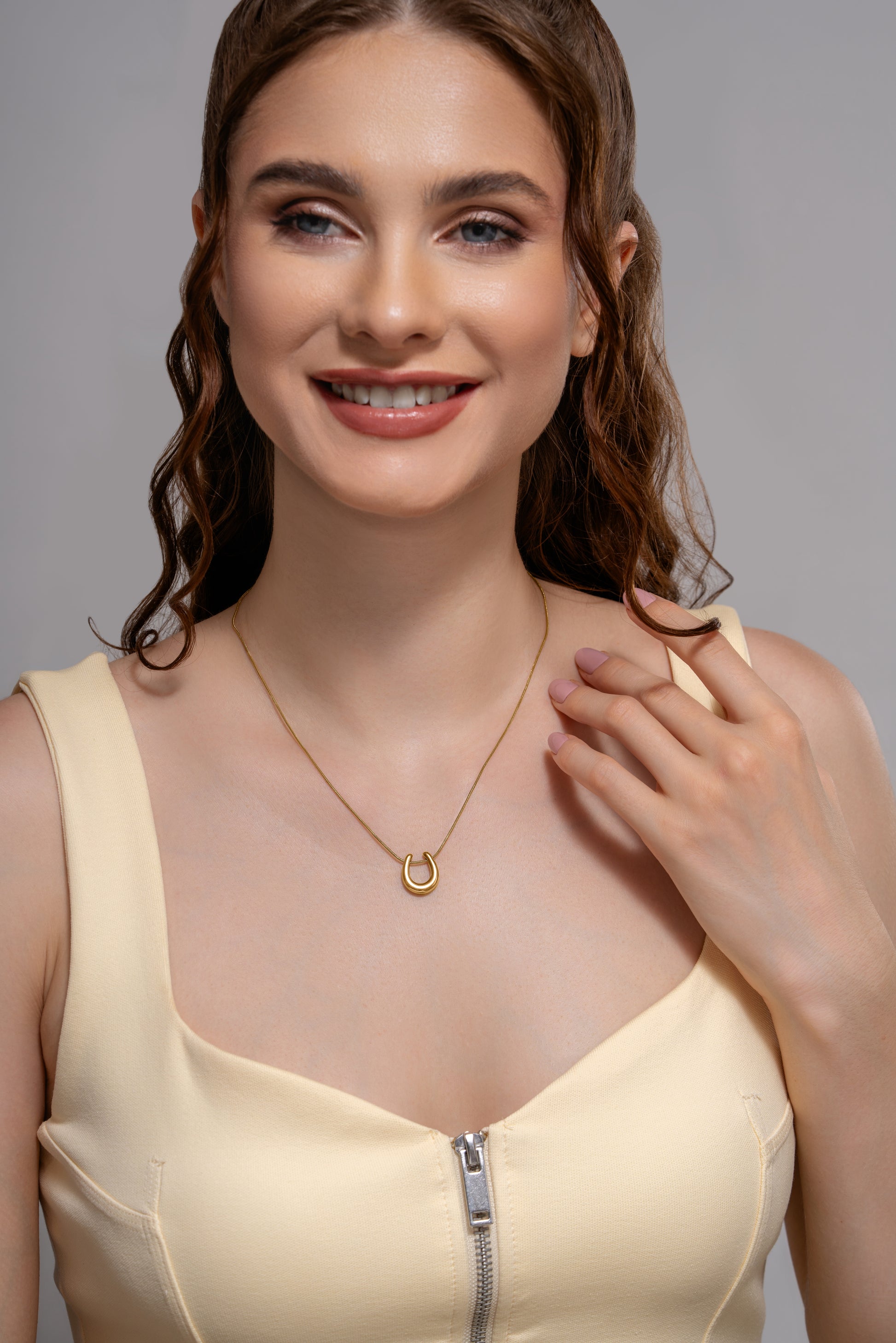 Model wearing the Luna Charm Necklace, featuring a delicate gold crescent pendant, styled with a cream zip-front dress.