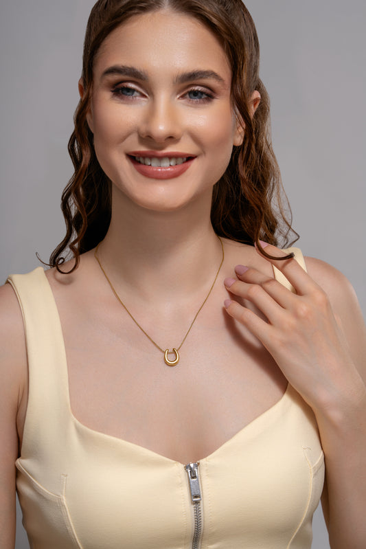 Model wearing the Luna Charm Necklace, featuring a delicate gold crescent pendant, styled with a cream zip-front dress.
