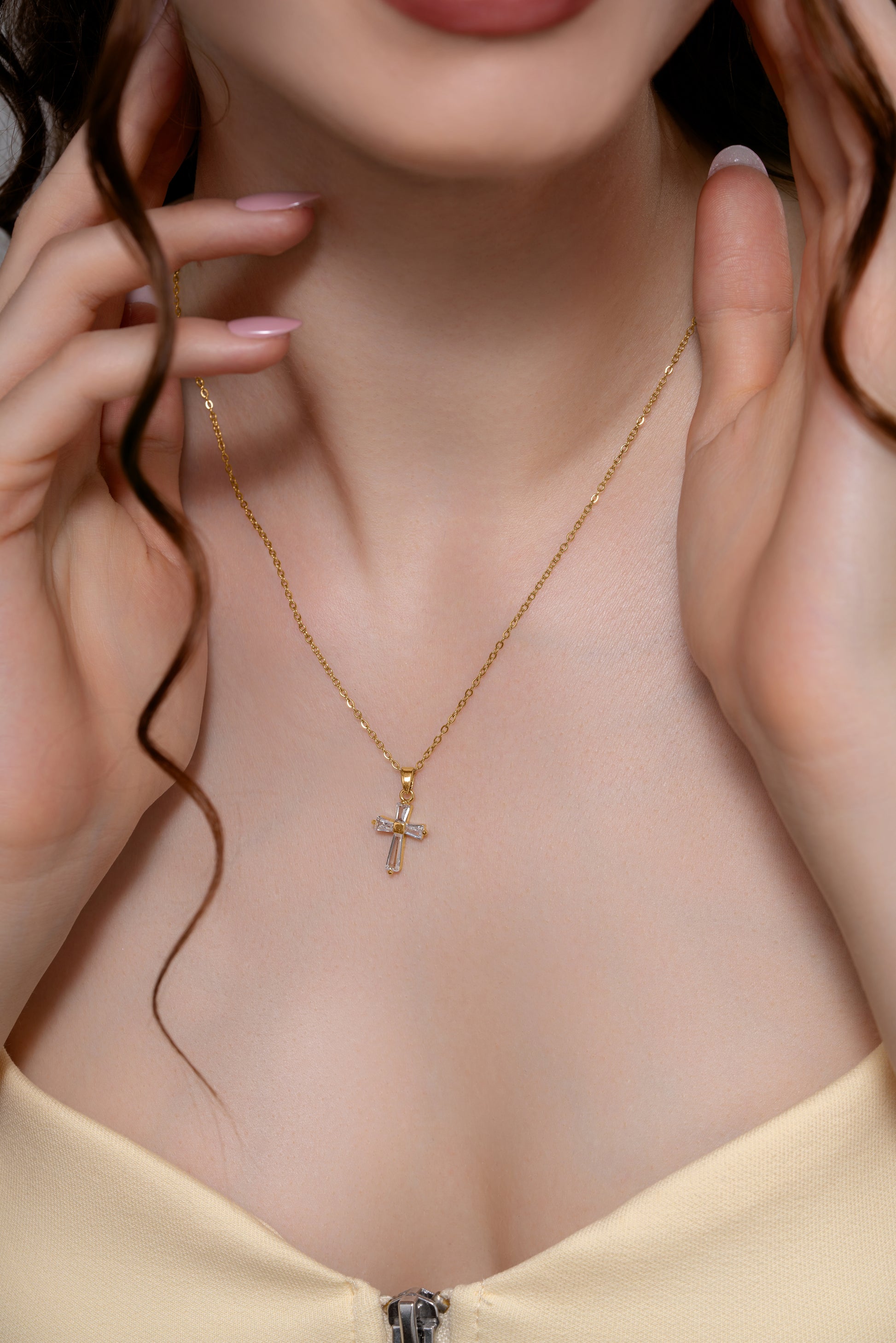 Close-up of a woman wearing a gold baguette pendant necklace, showcasing its delicate cross design and fine craftsmanship.