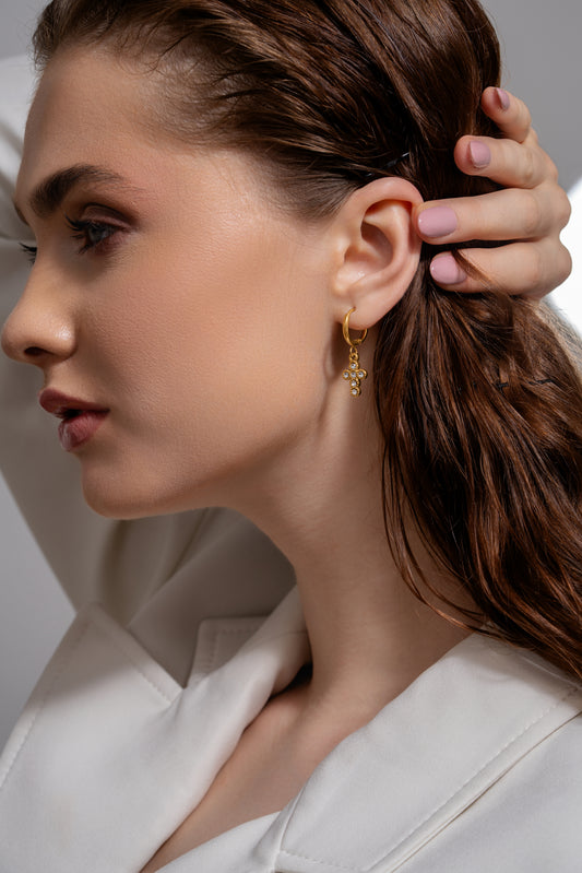 Model wearing gold cross earrings with gemstone accents, showcasing their size and fit for fashion-forward styling.