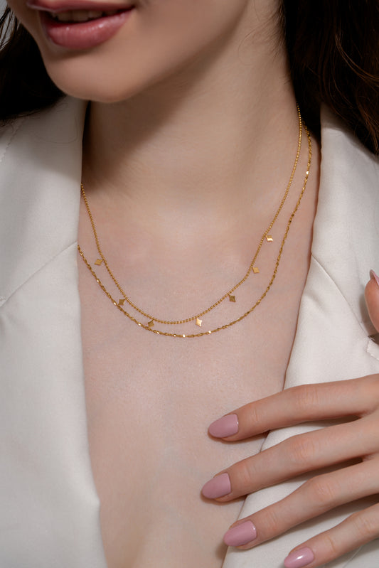 Model wearing Dusk Gleam Layered Chain necklace with gold-toned layers and diamond-shaped charms, styled with a white blouse for a chic look.