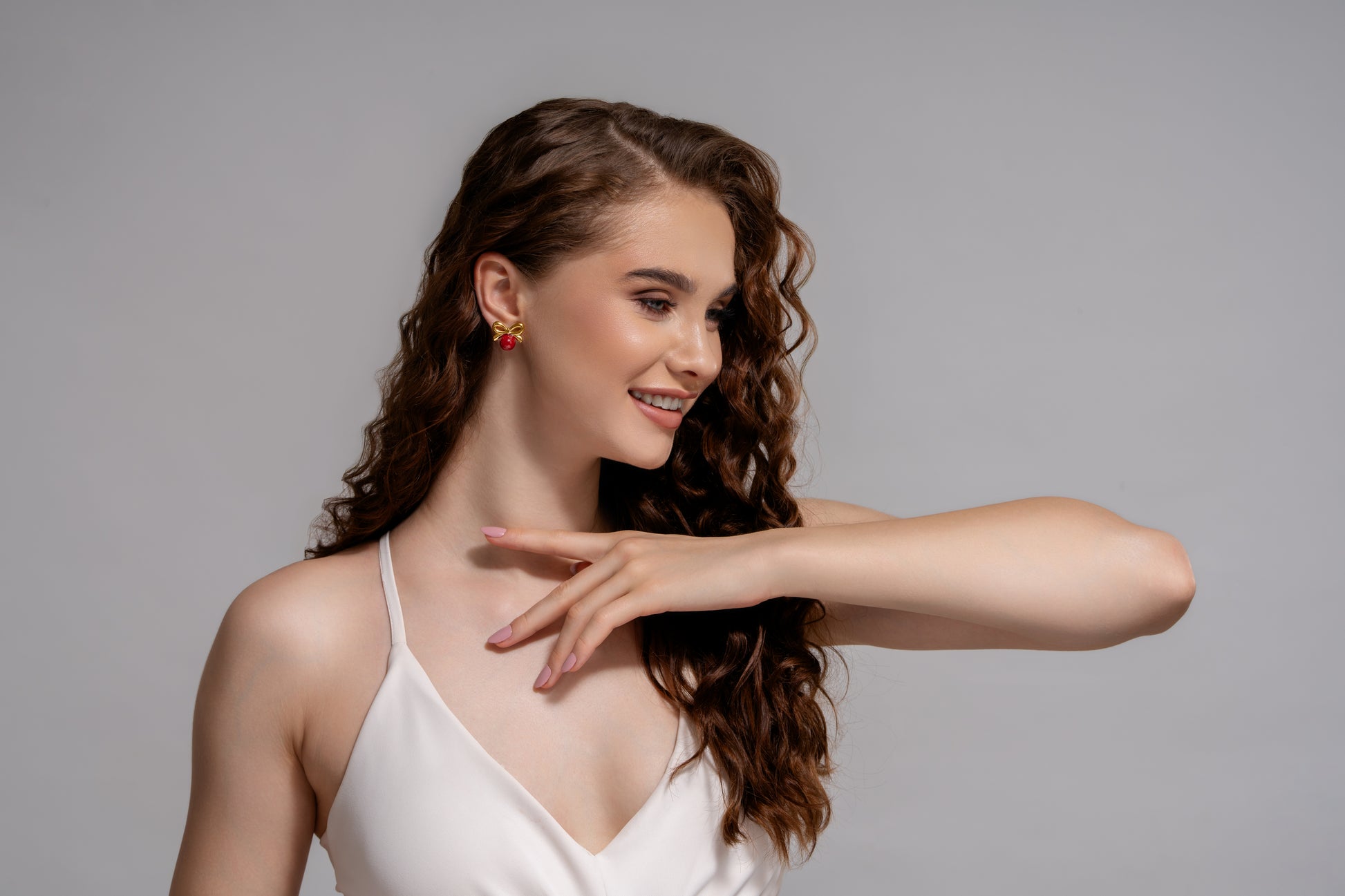 Smiling model in white outfit wearing Red Orb & Gold Bow Stud Earrings, highlighting their bold yet feminine appeal for formal or casual looks.