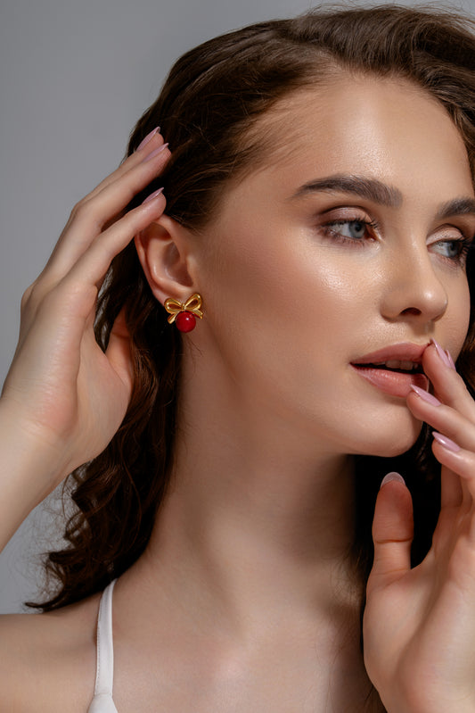 Model wearing Red Orb & Gold Bow Stud Earring, showcasing its chic design and vibrant color, perfect for stylish accessorizing.