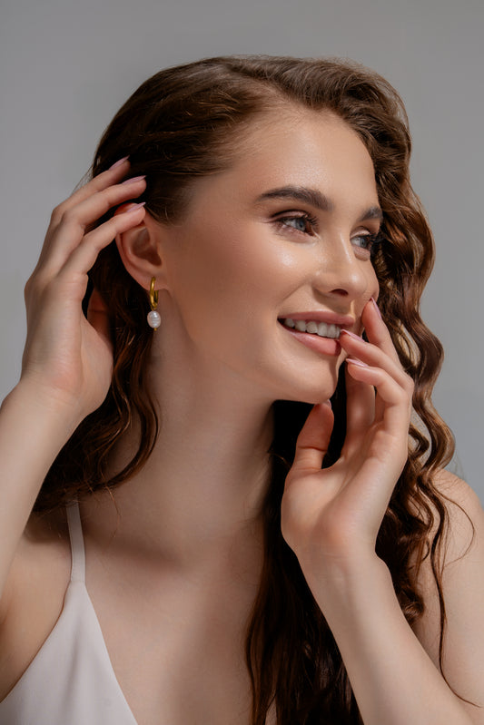 Model wearing Luna Pearl Drop Earrings, showcasing gold hoop design with dangling white pearls for a refined, stylish look.