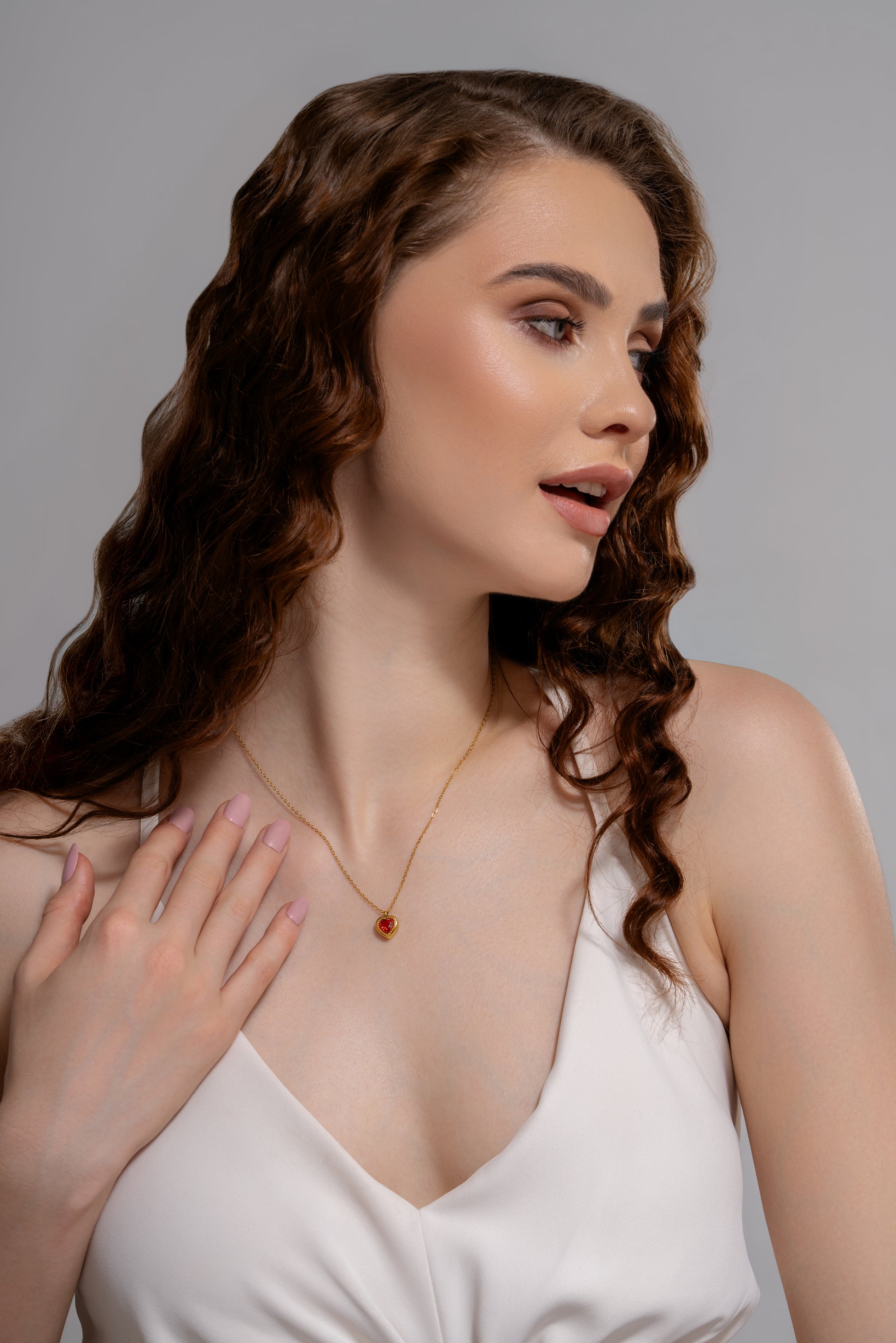 Model wearing the Crimson Heart Pendant with a red gemstone on a gold chain, styled with a white dress for an elegant jewelry look.