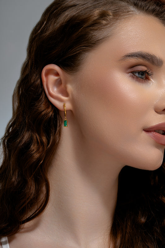 Model wearing Verdant Glow Emerald Drops earrings, showcasing elegant green emerald stones on gold hoops for a refined accessory look.