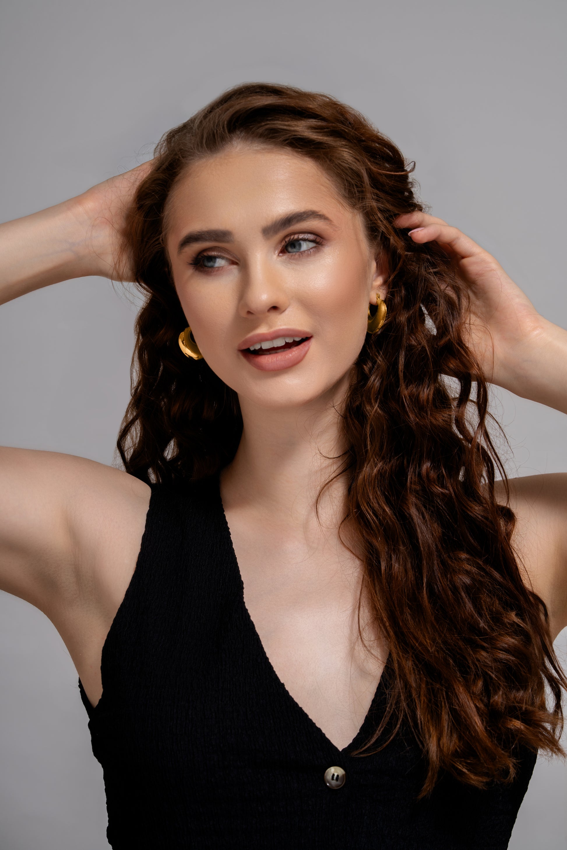 Luna Bold Gold Hoops styled on model with long wavy hair, highlighting their bold silhouette and luxurious gold tone.