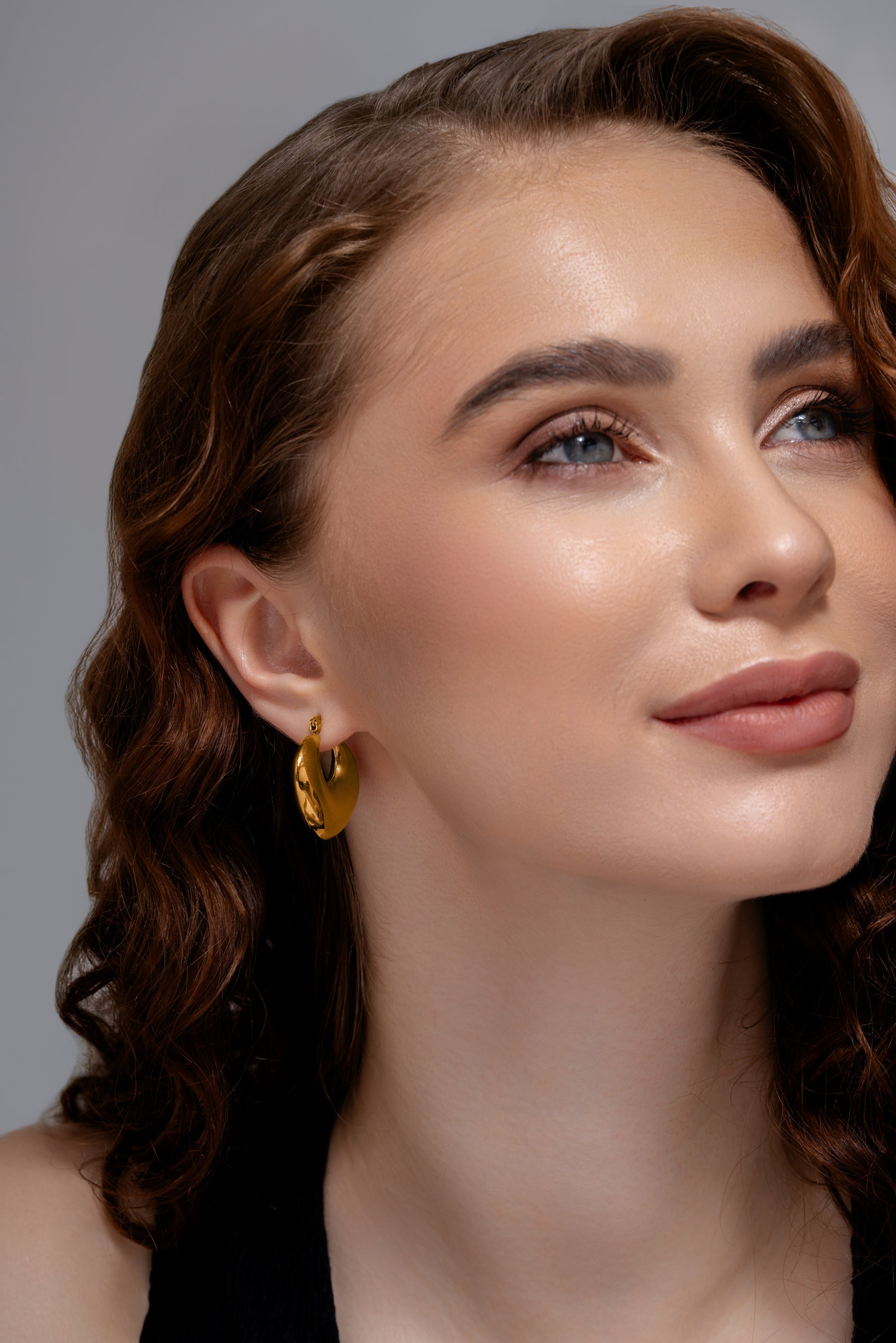 Close-up of model wearing Luna Bold Gold Hoops, emphasizing the earrings' smooth, reflective surface and sculptural shape.