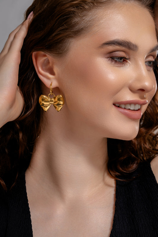 Model wearing Belle Bow Charm Earrings in gold, showcasing their bold, feminine design ideal for statement fashion looks.