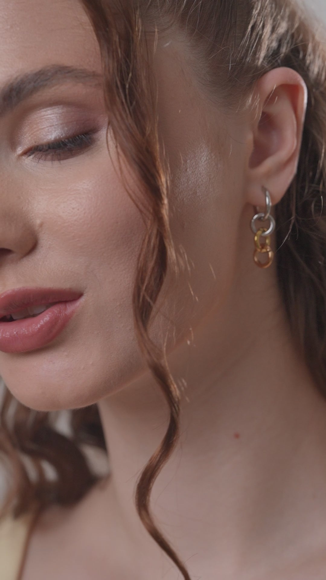 Zoomed-in view of Harmony Hoops earrings worn by model. Features silver, gold, and rose gold interlocking rings.