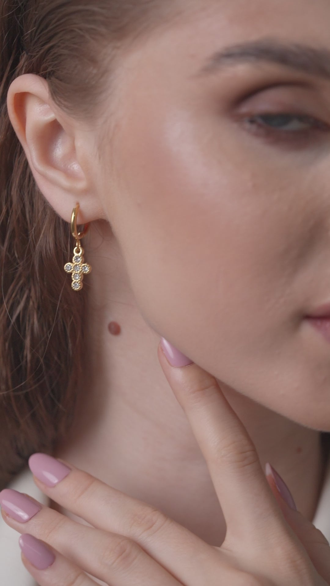 Close-up of gold cross earrings with sparkling stones worn by model, emphasizing luxurious detail and stylish appeal.