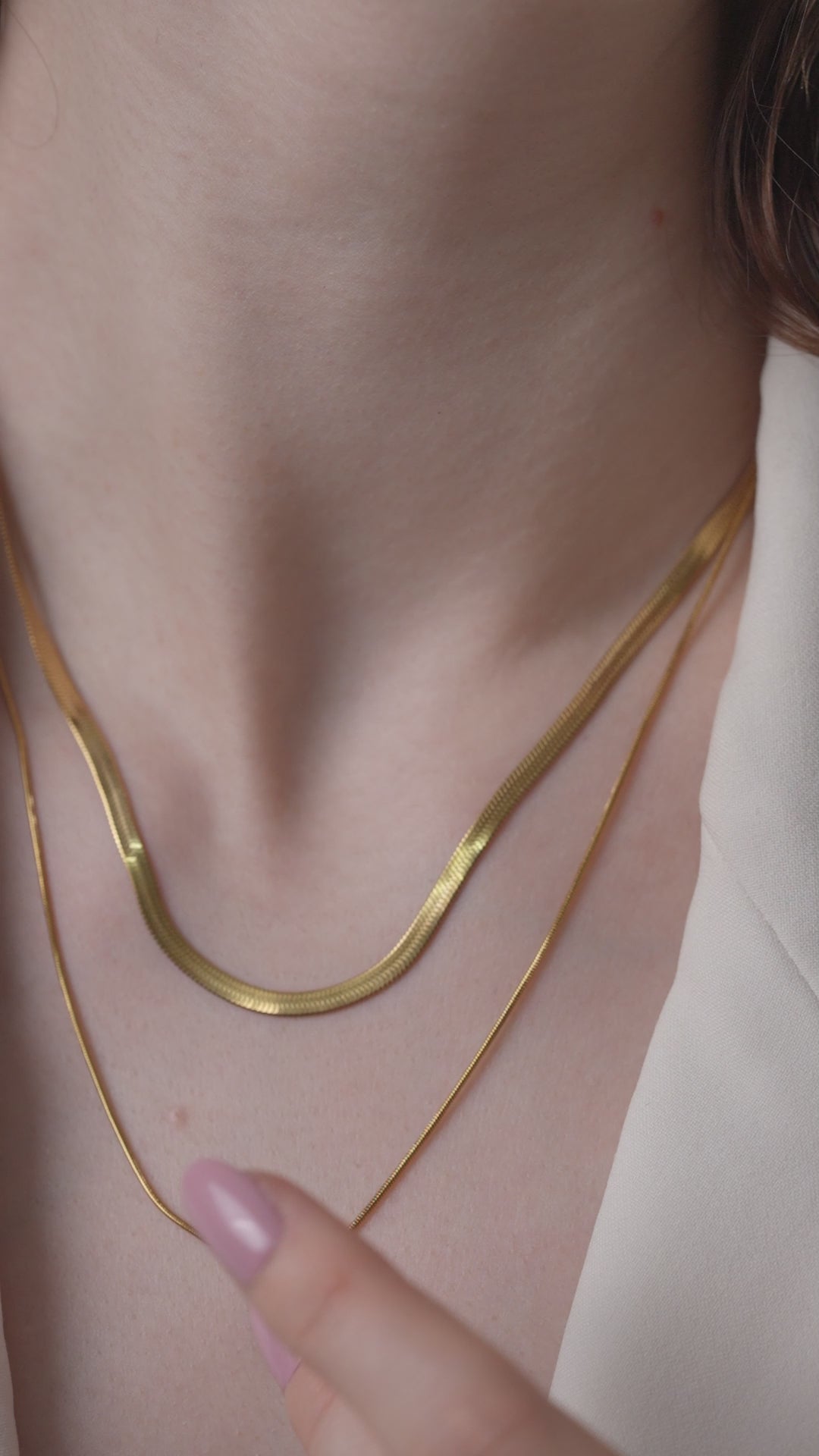 Layered Duo Necklace worn on the neck with a hand pointing at the gold chains, emphasizing the fine layered detailing and shine.