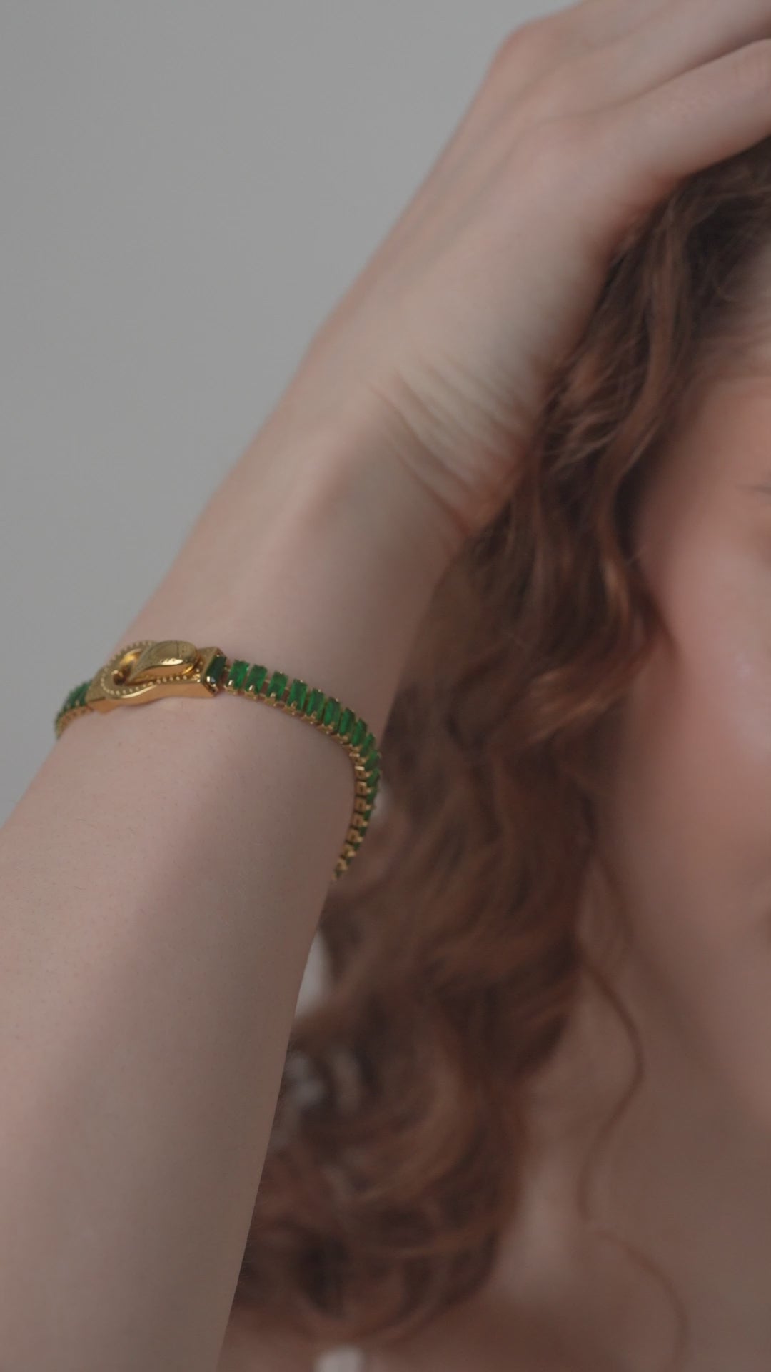 Emerald Baguette Tennis Bracelet on wrist, emphasizing the vivid green stones and gold buckle in a close-up fashion accessory shot.