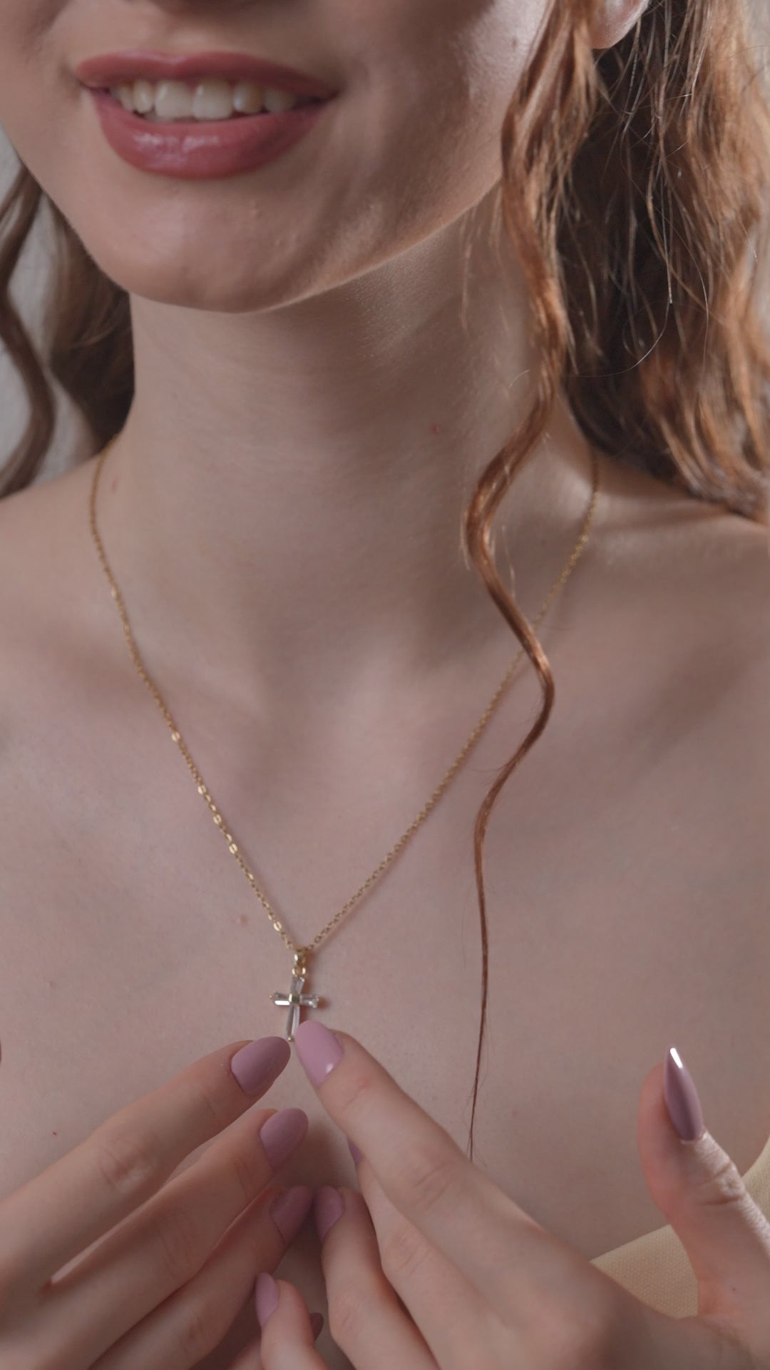 Woman gently touching a gold baguette pendant necklace, emphasizing the pendant's sparkling cross design and refined elegance.